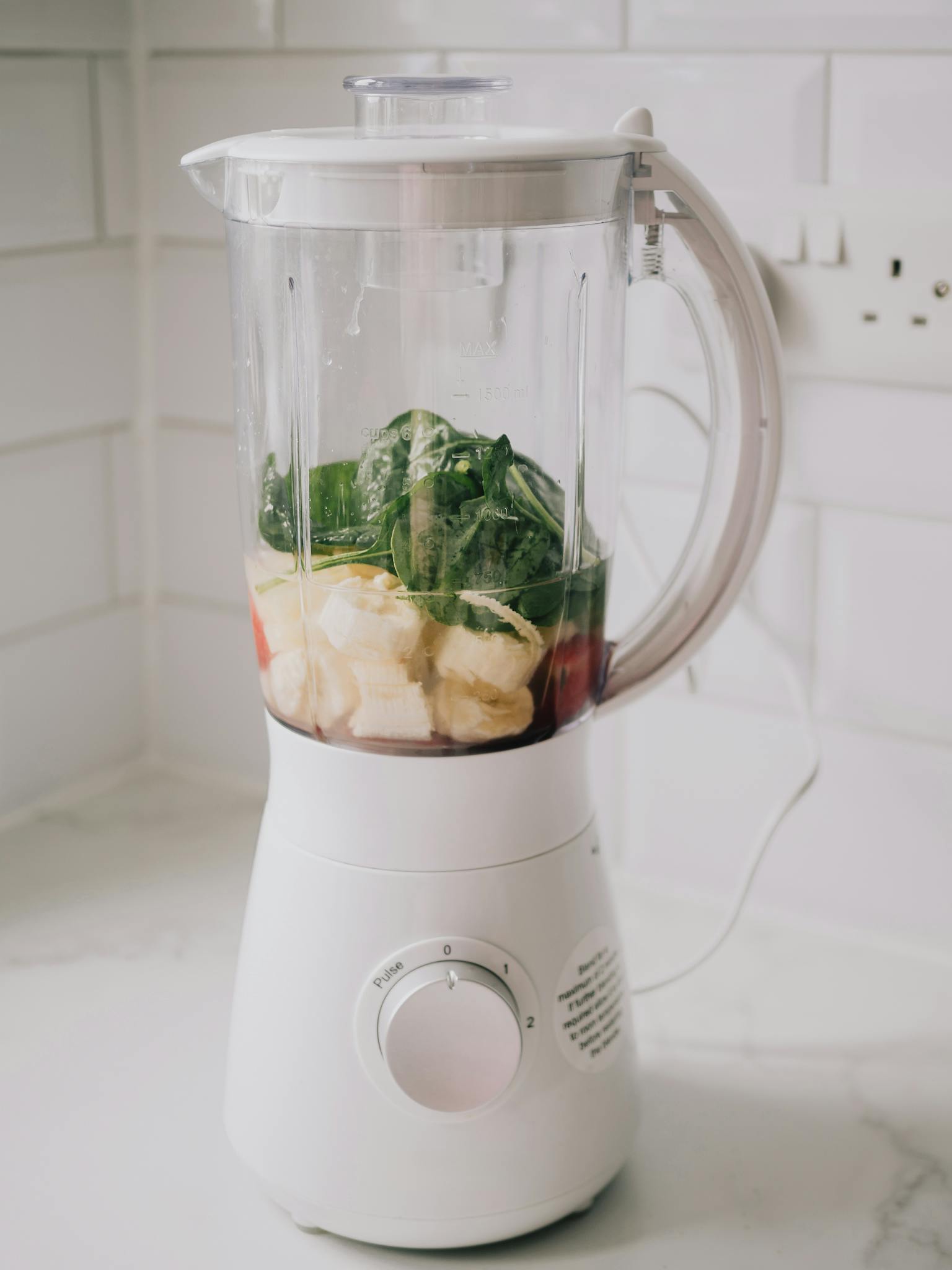 A blender filled with bananas, spinach, ready for a healthy smoothie.