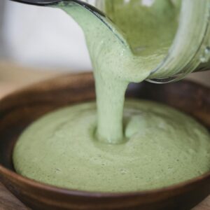 Close-up of creamy green smoothie being poured into a wooden bowl.