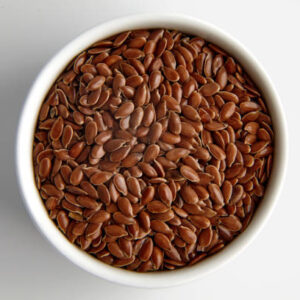 Flax seeds in a white ceramic bowl on a white background.