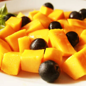 Closeup tasty fruits salad, fresh mangoes and grapes on white plate
