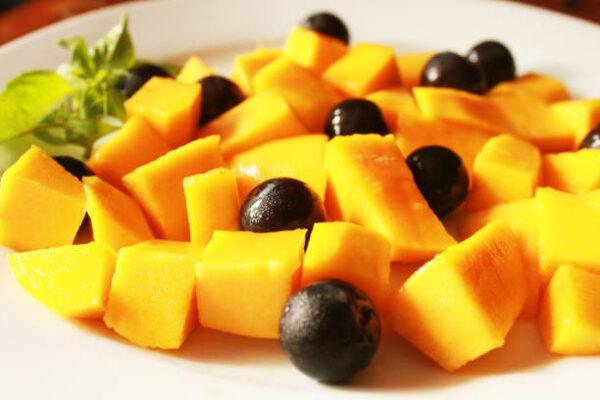 Closeup tasty fruits salad, fresh mangoes and grapes on white plate
